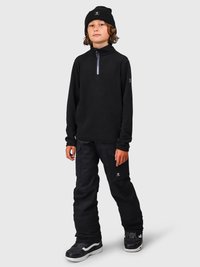 Bambino che indossa un berretto nero, una felpa nera con zip, pantaloni cargo neri e sneaker nere, in piedi su uno sfondo grigio uniforme.