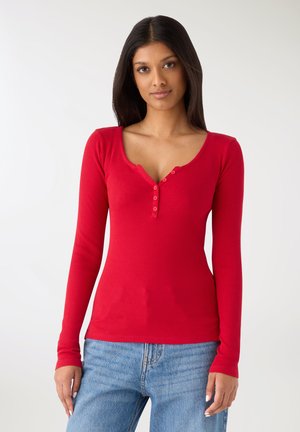 Czerwony top z długim rękawem wykonany z prążkowanej tkaniny, z dekoltem w serek i zapięciem na guzik przy szyi oraz dopasowanym krojem.