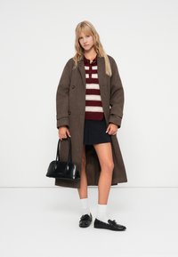Brun hørfrøjakke med store knapper, rød- og hvidstribet sweater, marineblå nederdel, sort taske, hvide sokker og sorte sko.