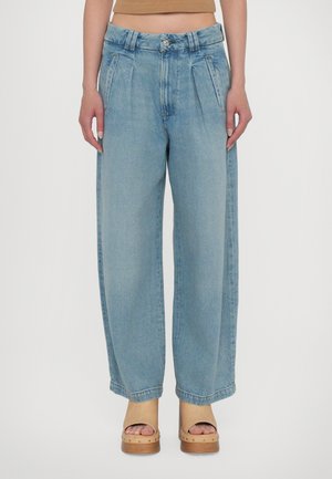 Light blue wide-leg jeans with pleats, high waist, and five-pocket design. Worn with wooden platform clogs, featuring rounded toe and strap.