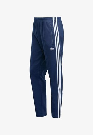 Calças de treino azul-marinho feitas de tecido macio, com três riscas verticais brancas nas laterais e um bolso com fecho na anca direita.