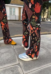 Veelkleurige patroonbroeken met diverse ontwerpen en texturen, gecombineerd met gele en lichtblauwe sneakers met witte accenten.