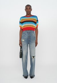 Multicolored knit crop sweater with short sleeves, paired with light blue high-waisted flared jeans featuring distressed detail and button fly.