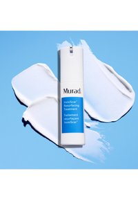 Traitement resurfçant InvisiScar de Murad dans un flacon pompe blanc sur un fond bleu, entouré de traces de crème blanche.