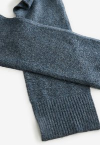 Écharpe en laine bleu foncé avec un tricot texturé. Les extrémités sont côtelées, offrant un contraste avec la surface douce et duveteuse du corps.