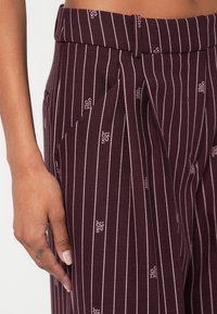 Bordeauxkleurige, op maat gemaakte broek met subtiele verticale strepen en geperste logo's, voorzien van een geplooid voorpand en een gladde textuur.