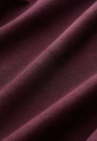 Tejido burdeos con un tejido texturizado, que muestra pliegues caídos que destacan el peso y la estructura del material.