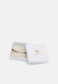 Cartera de cuero beige con una solapa redondeada, asegurada por un broche de metal, dentro de una caja blanca marcada con "GINETTE NY" en dorado.