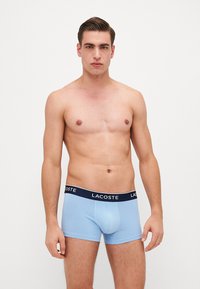Boxers ajustados de color azul claro con una cinturilla navy que presenta el logo de Lacoste. Textura suave, diseño ceñido y longitud a nivel del muslo.