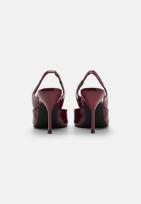 Burgundské lakované kožené sandále na vysokom opätku so slingback dizajnom, špicatou špičkou a textúrovaným remienkom. Čierne podrážky.