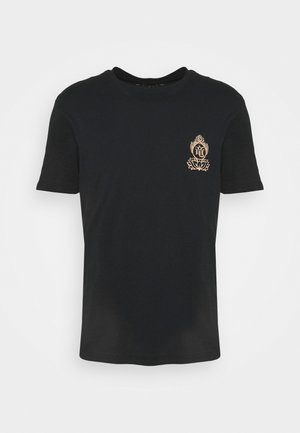 Schwarzes T-Shirt mit kurzen Ärmeln und kleinem goldfarbenem Lotus- und Flammenemblem mit einem asiatischen Schriftzeichen auf der linken Brustseite.
