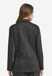 Szary marynarka w wzór jodełki z klapami, długimi rękawami i gładką strukturą, charakteryzująca się dopasowanym fasonem i czystymi liniami z tyłu.