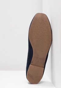 Zapato de ante azul marino con suela de goma texturizada. La suela presenta un patrón geométrico para mayor agarre y un diseño de tacón plano.
