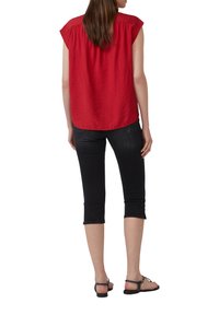 Czerwona bluzka z krótkim rękawem o luźnym kroju, zestawiona z czarnymi spodniami typu capri. Bluzka ma teksturowane wykończenie i okrągły dół.