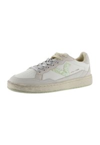 Sneaker bianca in pelle con accenti beige, suola testurizzata, lacci argentati e un logo verde scintillante. Presenta perforazioni sulla punta.