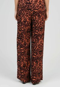Pantalons à large jambe orange avec un motif abstrait noir. Fabriqués en tissu lisse, avec une coupe décontractée et une longueur au sol.