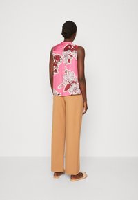 Ärmlös rosa blus med blommönster, som matchas med bruna vida byxor. Slippers fullbordar outfiten.