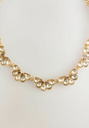 Aukso tono kaklo papuošalas, turintis ašaros formos skaidrius kristalus, surinktus lapo formos raštu, su blizgiais metaliniais akcentais ir jungtimis.