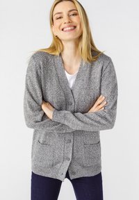 Cardigan grigio realizzato in tessuto a maglia testurizzato, con scollo a V, chiusura a bottoni e due tasche frontali. Indossato sopra un top bianco.
