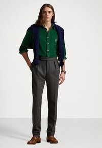 Πράσινο πουκάμισο με κουμπιά, μπλε πλεκτό γιλέκο, γκρι πλισέ παντελόνια, καφέ δερμάτινα παπούτσια. Απλός σχεδιασμός με υφασμάτινη υφή και εφαρμοστή γραμμή.