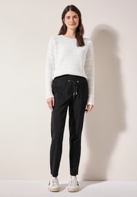 Pantalons noirs à cordon de serrage avec poches latérales, associés à un pull en tricot blanc avec un design en maille ouverte texturé. Des baskets blanches complètent le look.