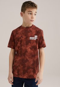 Brązowy t-shirt tie-dye z krótkimi rękawami, okrągłym dekoltem i białym nadrukiem przedstawiającym palmy oraz tekst "PRZYGODA CZKA".