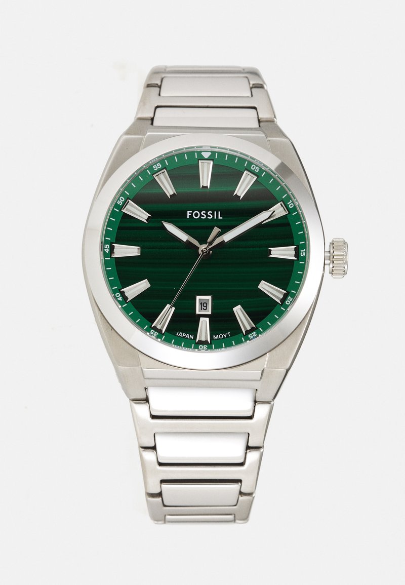 Montre Fossil avec un cadran rayé vert, des index en argent, une fonction date à 6 heures et un bracelet en acier inoxydable avec des accents blancs.
