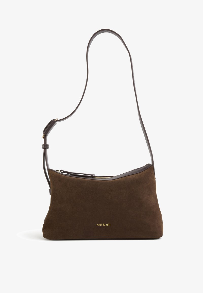 Sac à bandoulière en daim marron avec une sangle en cuir foncé et un logo doré. Dispose d'une fermeture éclair et d'une forme douce et structurée.