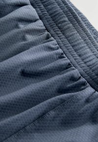 Gros plan sur un tissu bleu marine avec une ceinture élastique et un motif en quadrillage texturé sur un short léger.