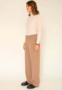 Pull col roulé beige côtelé associé à un pantalon large kaki. Des mocassins marron foncé à la finition texturée complètent la tenue.