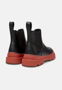 Svarta läder Chelsea-stövlar med elastiska sidopaneler, med en tjock röd gummisula och dragflik vid hälen. Ren, modern design.