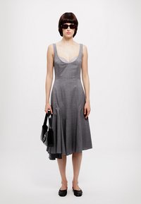 Rochie gri fără mâneci, cu un corset ajustat și fustă evazată, realizată dintr-un material texturat. Modelul poartă o geantă neagră și pantofi fara toc.