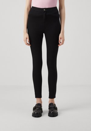 Jean skinny noir à taille haute, fabriqué en denim extensible. Il présente une fermeture à bouton sur le devant et un design lisse et ajusté.