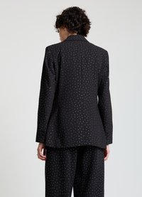 Schwarzer Blazer mit weißen Polka-Dots, strukturierter Schnitt, Reverskragen, sichtbare Rückennaht, kombiniert mit passenden Hosen für einen koordinierten Look.