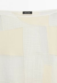 Kremowo-biały patchworkowy materiał o różnorodnych fakturach tkanin z czarną metką wszytą na środku u góry z napisem Massimo Dutti.