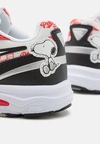 Zapatillas en blanco y negro con un gráfico de Snoopy, detalles rojos, rayas plateadas y una suela texturizada para mayor agarre.