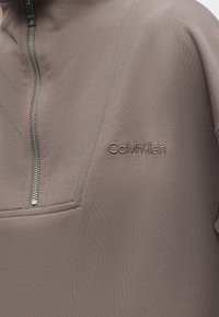 Πουλόβερ Calvin Klein σε απόχρωση ταουπ με ασημί φερμουάρ στο ένα τέταρτο και διακριτικό κεντημένο λογότυπο στην αριστερή πλευρά του στήθους.