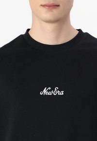 Black cotton t-shirt with a classic crew neck, featuring white embroidered "New Era" logo on the chest. Smooth texture and fitted design.