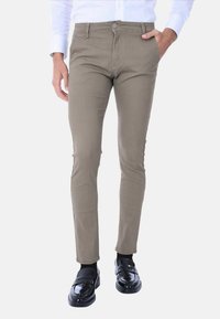 Pantaloni slim fit color khaki con superficie testurizzata, dotati di tasche frontali e chiusura con bottone, indossati con mocassini neri.