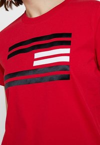 Camiseta roja con tres franjas horizontales: dos negras y una blanca, creando un diseño gráfico audaz en la parte frontal.