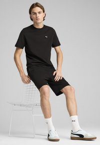 Black cotton t-shirt with small logo, paired with black shorts. White socks with logo and multicolored sneakers complete the outfit.