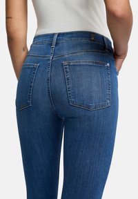 Blå denimjeans med midjelång midja, klassisk femficksdesign och subtil sömnad längs sömmarna och fickorna.