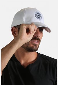 Casquette de baseball blanche avec un logo circulaire noir à l'avant. Tissu lisse, visière incurvée et fermeture arrière ajustable.