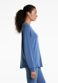 Niebieska oversize bluza, długie rękawy, okrągły dekolt, miękka tekstura, zestawiona z pasującymi niebieskimi legginsami, minimalistyczny design, brak widocznych logo.