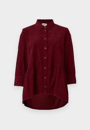 Camisa de côr bordô em veludo cotelê com colarinho clássico, fecho dianteiro em botões e mangas de três quartos; apresenta uma bainha peplum e tecido texturizado.