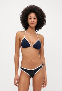 Námornícky bikiny set vyrobený z hladkej tkaniny. Vrchná časť má trojuholníkový dizajn s bielym lemom; spodná časť má podobný štýl s kontrastnými akcentmi.