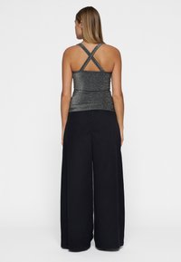 Metallic grijzige tanktop met kruislings straps op de rug, gecombineerd met loszittende zwarte broek. Gladde textuur met een smal ontwerp.