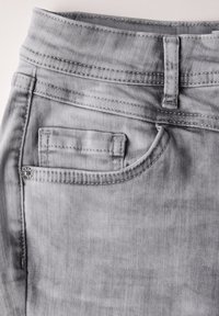 Tejido de mezclilla gris con una textura suave, que presenta un pequeño bolsillo delantero y un bolsillo trasero más grande, con costuras decorativas a lo largo de la cintura.