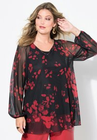 Blusa nera trasparente con stampa floreale rossa, scollo a V, maniche lunghe e design fluido. Abbinata a pantaloni rossi per un look coordinato.