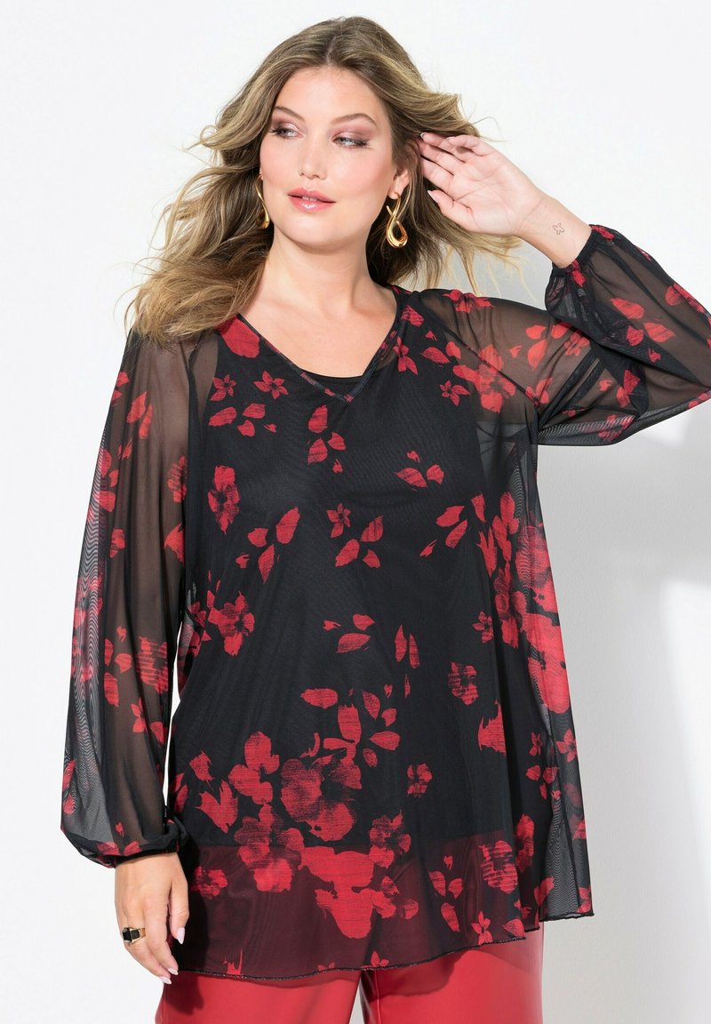 Blusa nera trasparente con stampa floreale rossa, scollo a V, maniche lunghe e design fluido. Abbinata a pantaloni rossi per un look coordinato.